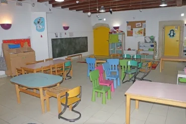 Une salle avec des tables et chaises, un tableau noir et des rangements pour des enfants de 4 à 6 ans