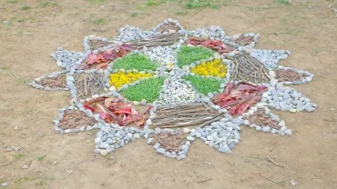 Des éléments naturels (pierres, écorces, branches, feuilles, fleurs, herbes) sont disposés sur le sol en forme de mandala étoilé