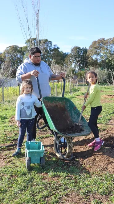 Deux enfants et un animateur avec une brouette mettent du compost au pied d'un arbre