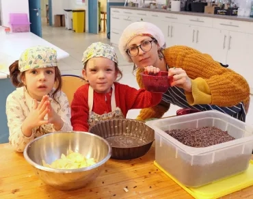 Une animatrice et deux enfants en tablier et charlottes montrent les fruits pour leur préparation culinaire