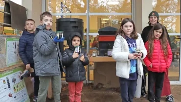 un groupe d'enfants et leur animatrice sont devant les vermicomposteurs et montrent des bocaux de thé de vers