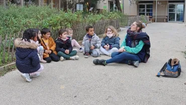 un groupe d'enfant assis par terre écoute une animatrice