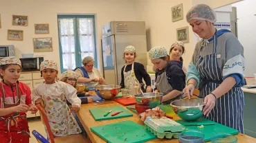 un groupe d'enfant et leurs animatrices avec charlottes et tabliers sont en cuisine 