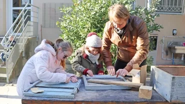 deux enfants et un adulte poncent du bois en extérieur