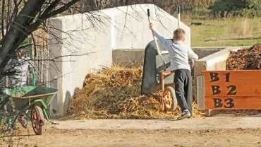 Un enfant vide une brouette de fumier sur un tas de compost dans une aire de compostage