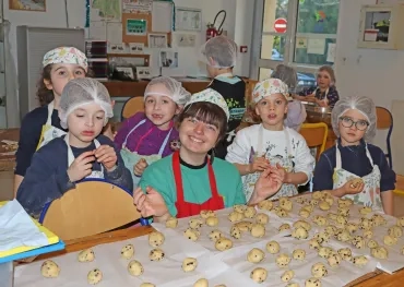 un goupe d'enfants et leur animatrice portent des charlottes et des tabliers pour former des boules de pâte à cookies