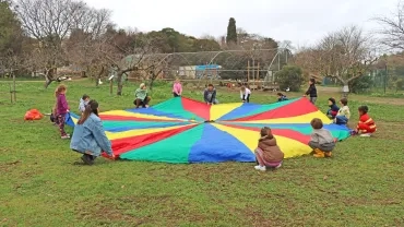 un groupe d'enfants et leurs animateurs sont autour d'un grand tissu rond et coloré