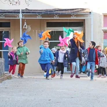 un goupe d'enfants et leur animatrice courent avec un grand moulin à vent en papier dans la main