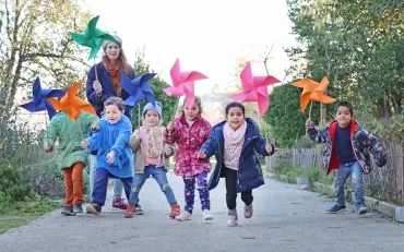 un goupe d'enfants et leur animatrice courent avec un grand moulin à vent en papier dans la main