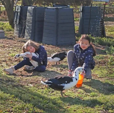 Deux enfants sont en compagnie de canards et une petite fille tient un canard dans ses bras