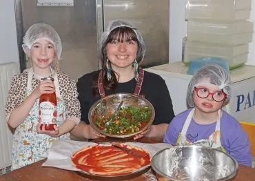 En cuisine, deux enfants et leur animatrice montrent la préparation qui servira aux pizzas