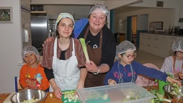 un goupe d'enfants et leurs animatrices portent des charlottes et des tabliers et coupent du poireau