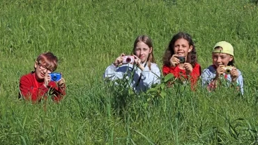 Un groupe d'enfants sont dans les herbes hautes avec des appareils photos à la main