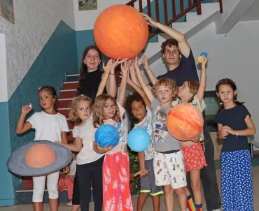 Un groupe d'enfants et deux animateurs posent avec des planètes et le Soleil