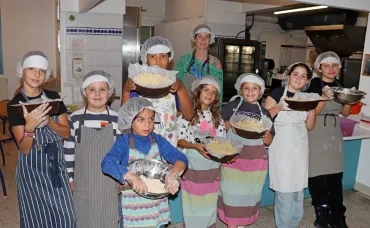 un groupe d'enfants et leur animatrice montrent des plats dans une cuisine
