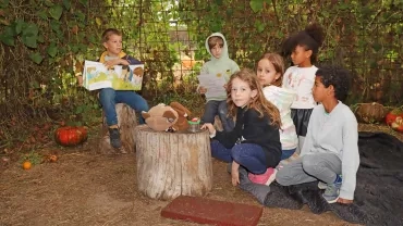 un groupe d'enfants est assis avec un livre sous le feuillage des courges
