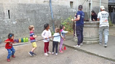 un groupe d'enfants et leurs animateurs tirent sur une corde devant un puits