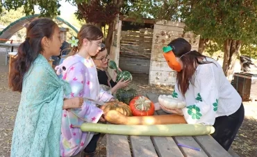 un groupe d'enfants et leur animatrice qui porte un masque orange portent des courges