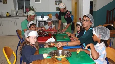 un groupe d'enfants et leurs animateurs coupent des légumes en cuisine