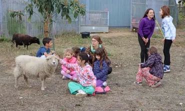 un groupe d'enfants et leur animatrice sont assis par terre avec des moutons