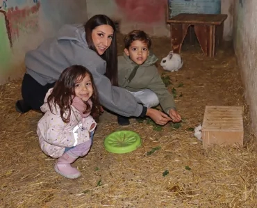 deux enfants et leur animatricent tendent de l'herbe à un cochon d'Inde