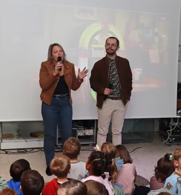 deux adultes parlent dans un micro devant un groupe d'enfants
