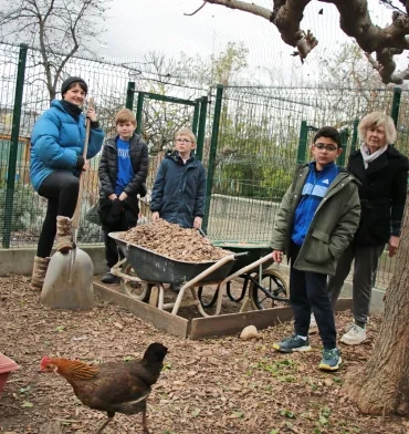 un groupe d'enfants et leurs animatrices posent avec une brouette pleine de paille avec une poule en premier plan