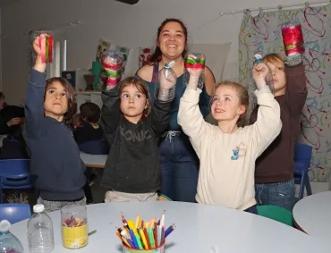 un groupe d'enfants et leur animatrice montrent des bouteilles en plastique coupées en deux