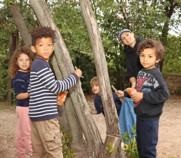 Un groupe d'enfants et leur animatrice peignent des troncs d'arbre