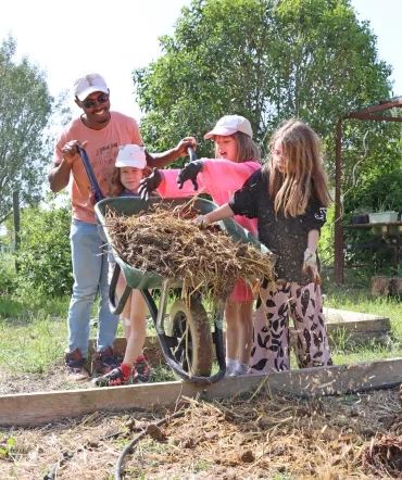 Un groupe d'enfants et leur animateur font tomber du fumier d'une brouette