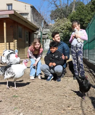 Un groupe d'enfants et leur animateur sont dans un poulailler avec des dindons et des poules