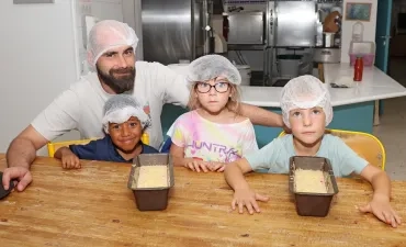 Un groupe d'enfants et leur animateur sont derrière des moules à cake remplies de pâte