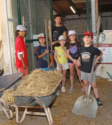 Un groupe d'enfants et leur animatrice posent avec des pelles derrière des brouettes remplies de paille