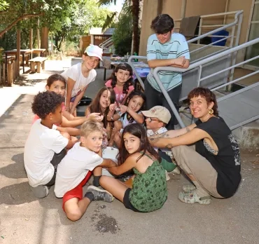 Un groupe d'enfants et leur animatrice sont assis par terre avec une bassine