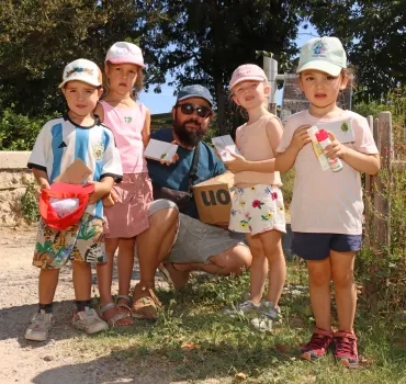 Un groupe d'enfants et leur animatrice montrent des morceaux de carton autocollant avec des éléments naturels collés dessus