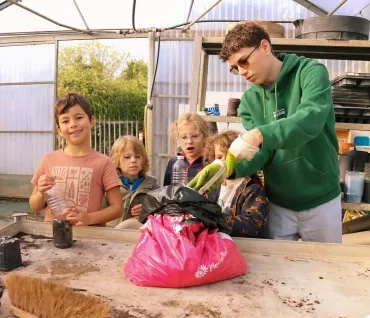 Un groupe d'enfants et leur animateur tiennent des bouteilles en plastique et versent de la terre dedans
