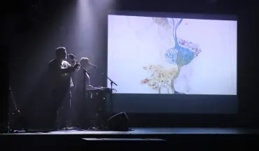 Deux adultes sur scène dans la pénombre avec un dessin projeté en vidéo