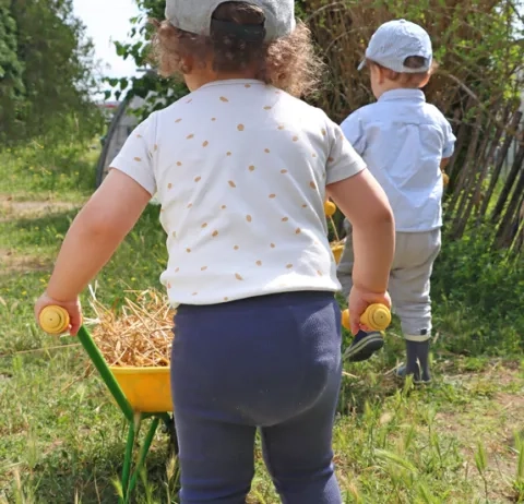 Deux enfants d'une crèche transportent de la paille avec des petites brouettes sur un chemin enherbé