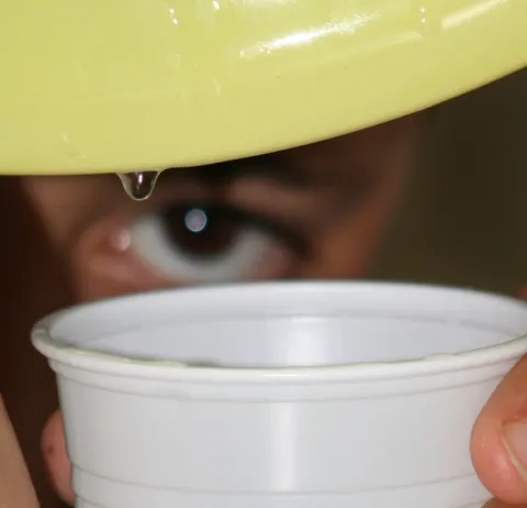 Une goutte d'eau coule d'une assiette avec un verre en dessous et l'œil d'un enfant derrière