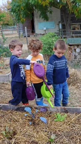 3 enfants dans un jardin avec des arrosoirs