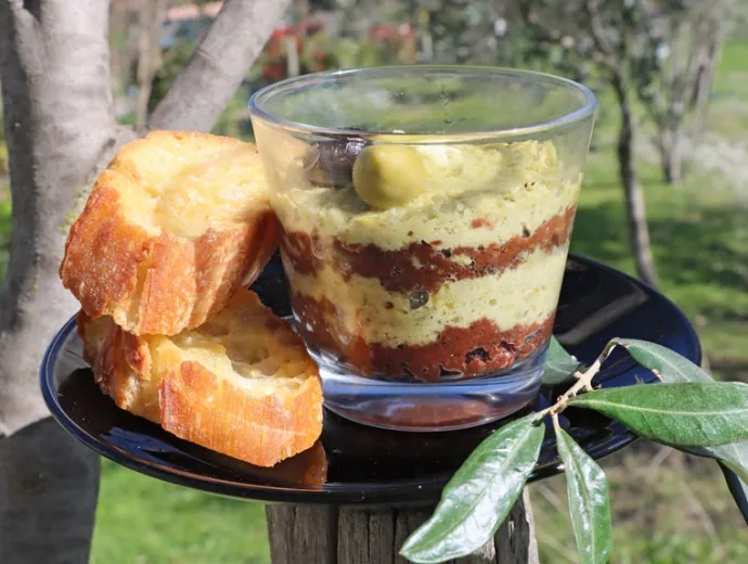 Une verrine de tapenade avec des couches noires et vertes avec deux tranches de pain grillées