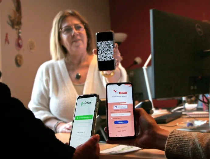 en premier plan deux smartphones avec l'application Graine et Ancv Connect et en arrière plan une agente qui montre un Qrcode sur son téléphone