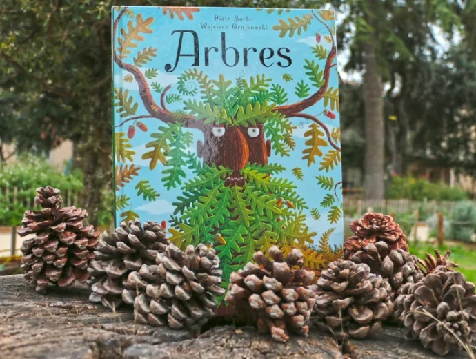 Le livre Arbres est exposé sur un grand tronc coupé et entouré de pommes de pin