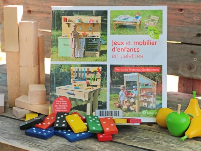 Le livre Jeux d'enfants en palettes est présenté face couverture entouré de jeux d'enfants colorés en bois