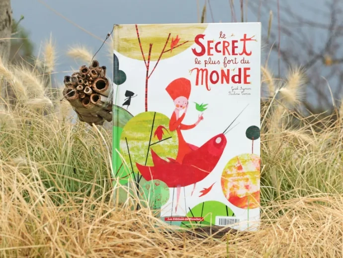 Le livre Le secret le plus fort du monde est exposé première de couverture, sur l'herbe jaunie. Un abri à abeille sauvages est posé contre le livre.