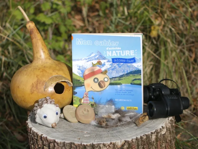 Le livre Mon cahier d'activités nature automne hiver est présenté sur un tronc entouré d'une paire de jumelles, et d'éléments naturels