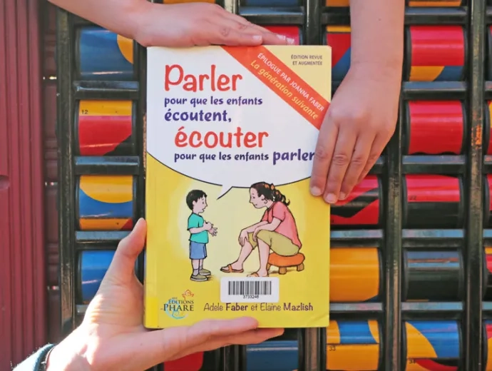 Le livre est présenté face première de couverture, maintenu par trois mains d'enfants 