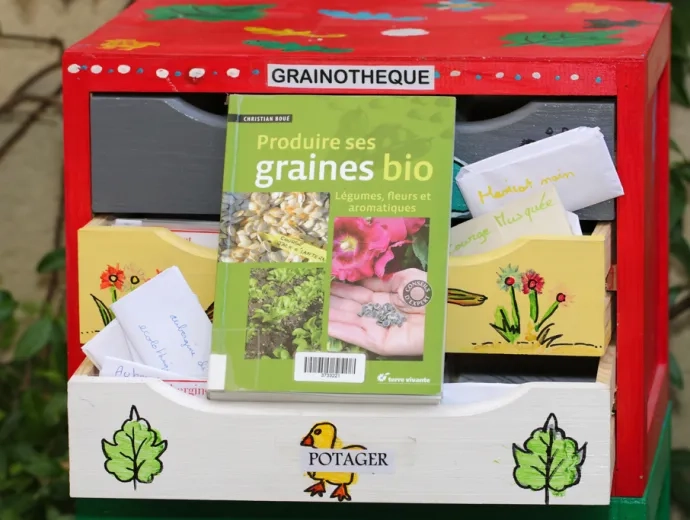 Le livre produire ses graines bio est exposé sur le tiroir ouvert d'une grainothèque