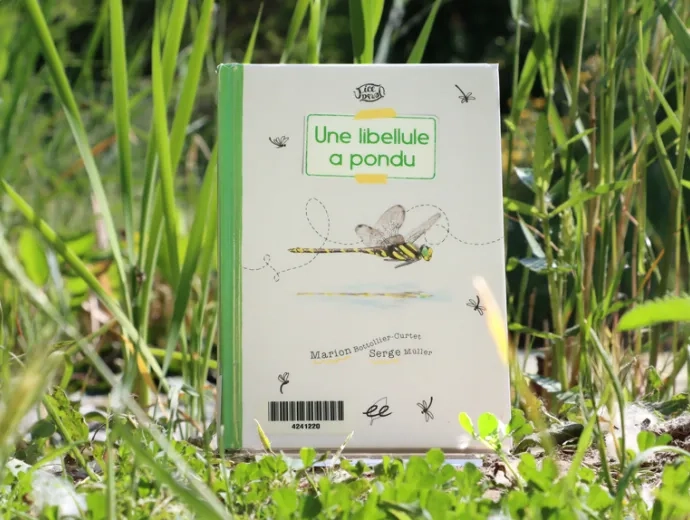 Le livre Une libellule a pondu est exposé au sol, dans l'herbe.
