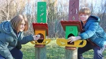 Deux enfants installent de la nourriture dans deux mangeoires à oiseaux